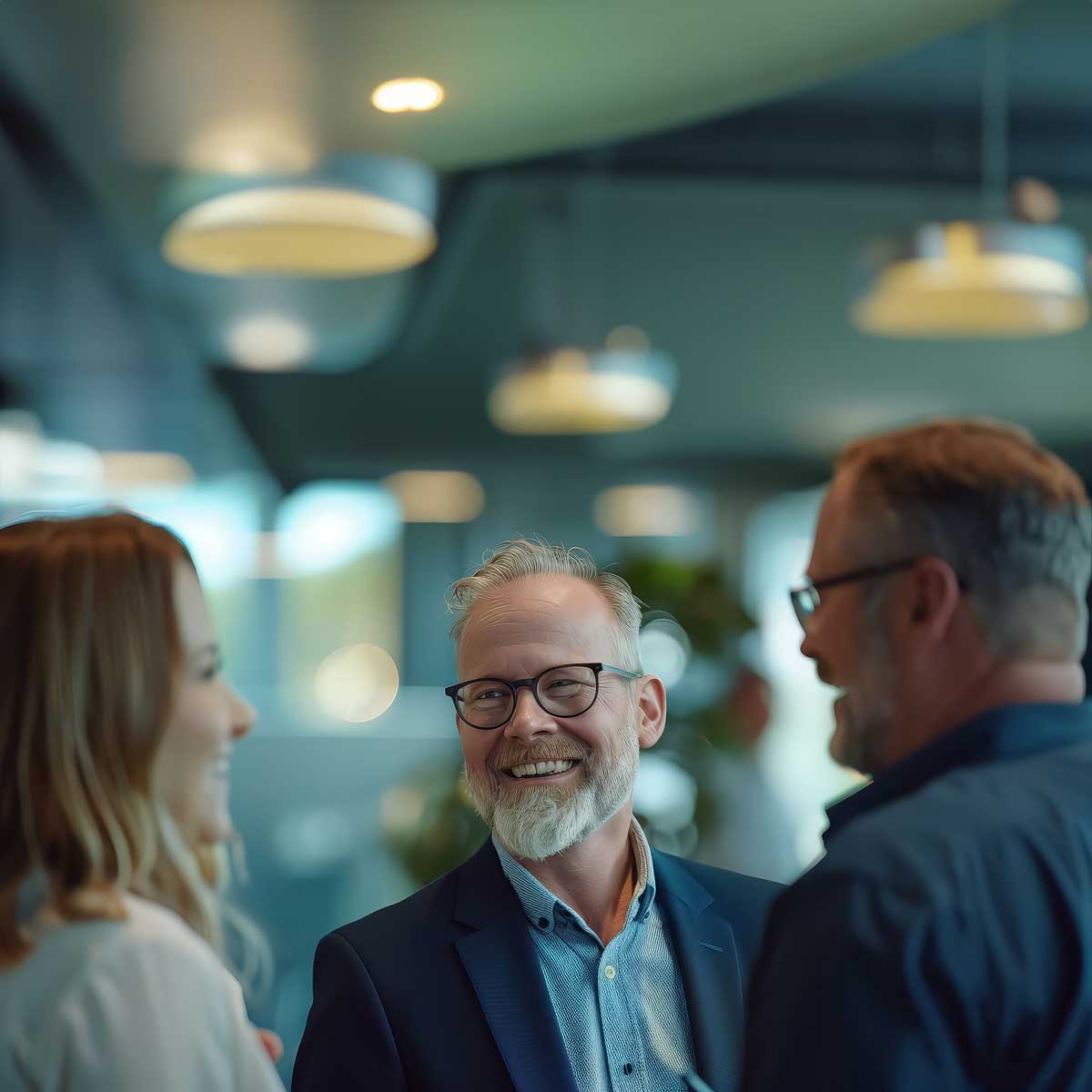 A cheerful group of business professionals engaged in a friendly conversation in a well-lit, modern office space. The image reflects collaboration, networking, and positive workplace interactions, ideal for promoting business, leadership, and team-building environments.