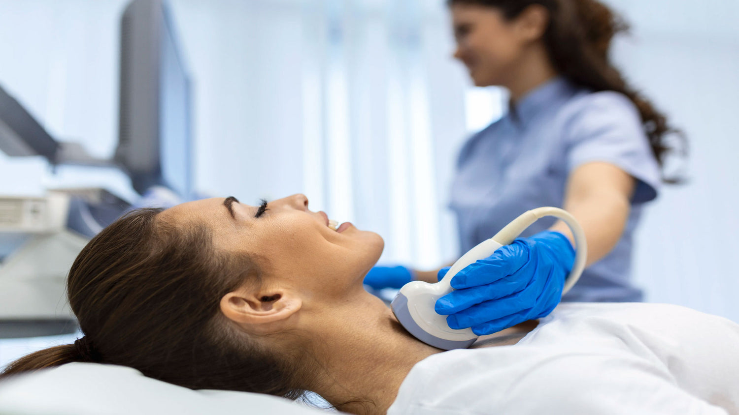 A woman undergoing a thyroid ultrasound scan while smiling, performed by a healthcare professional in a clinical setting.