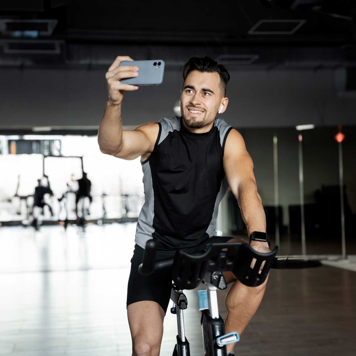 A man enjoys a workout on an indoor cycling machine, capturing the moment with a selfie. This image showcases an active, healthy lifestyle, perfect for promoting fitness, wellness, and personal health journeys while taking Mitochondrial support supplement.